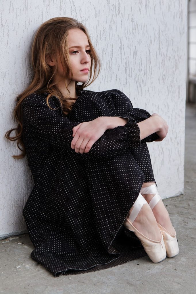 Woman in black dress sitting on ground and looks sad